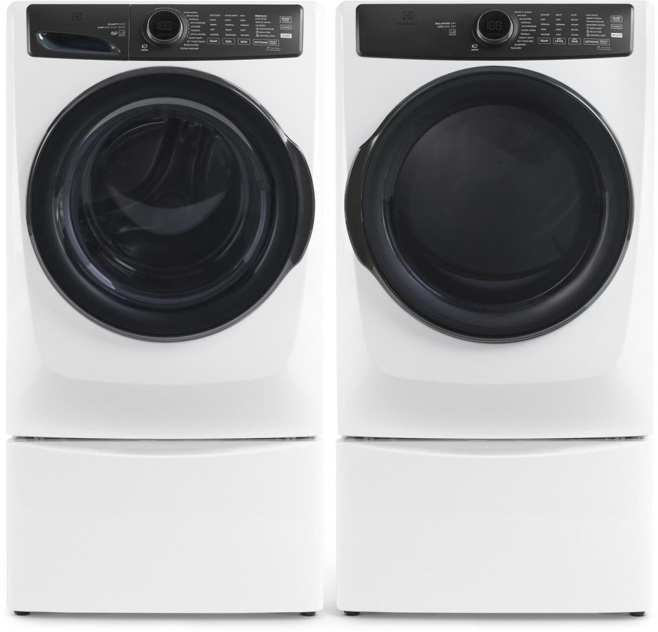 A white front-loading washer and dryer set, each with a digital display and control panel, placed side by side on matching pedestals for added height and storage.