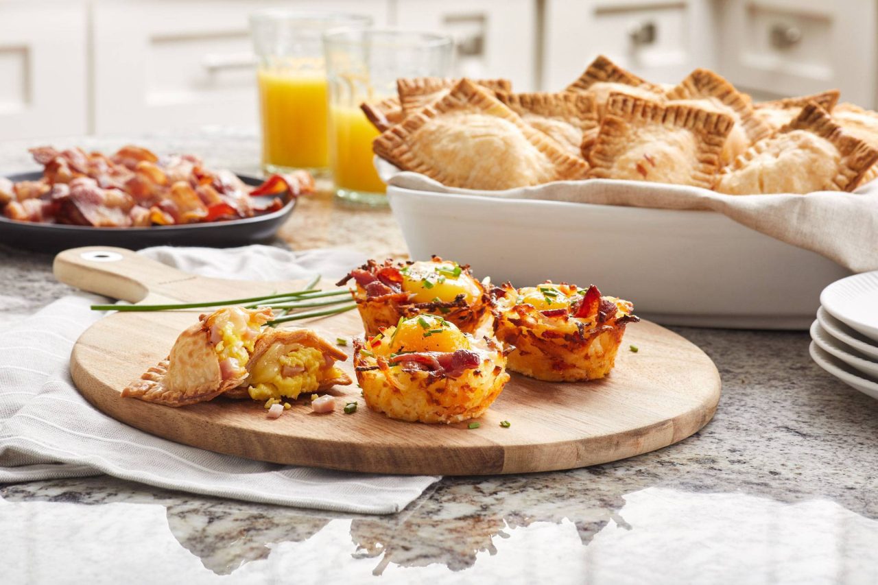 Close-up photograph of crispy breakfast hors d'oeuvres with a plate of bacon and glasses of bright orange juice.