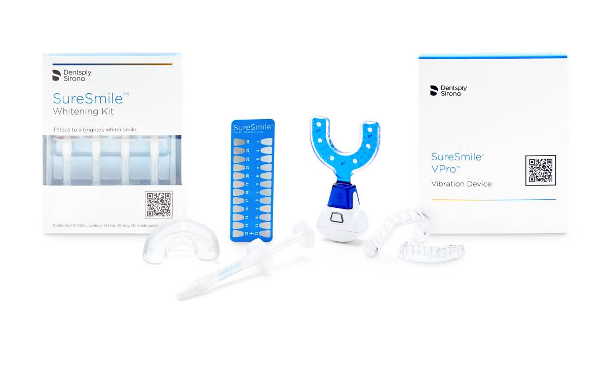 The image shows a SureSmile Whitening Kit and SureSmile VPro Vibration Device. The kit includes several clear dental trays, a blue LED light, a shade guide, and whitening gel, with the packaging displayed behind the products.