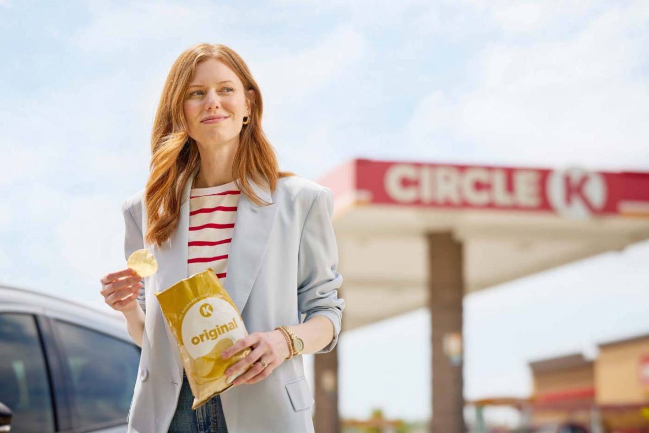 Lifestyle photograph of a smiling woman eating chips outside a gas station.