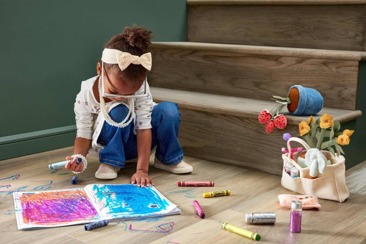 Photograph of a young child sitting at the bottom of a staircase coloring in a book with bright crayons.