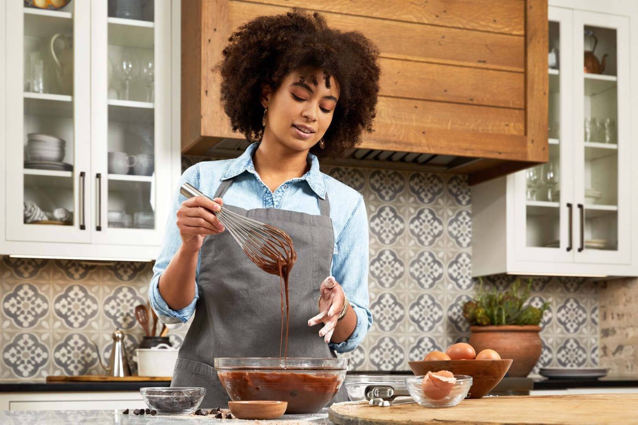 Lifestyle photograph of a home cook in the kitchen whisking chocolate cake batter in an apron.