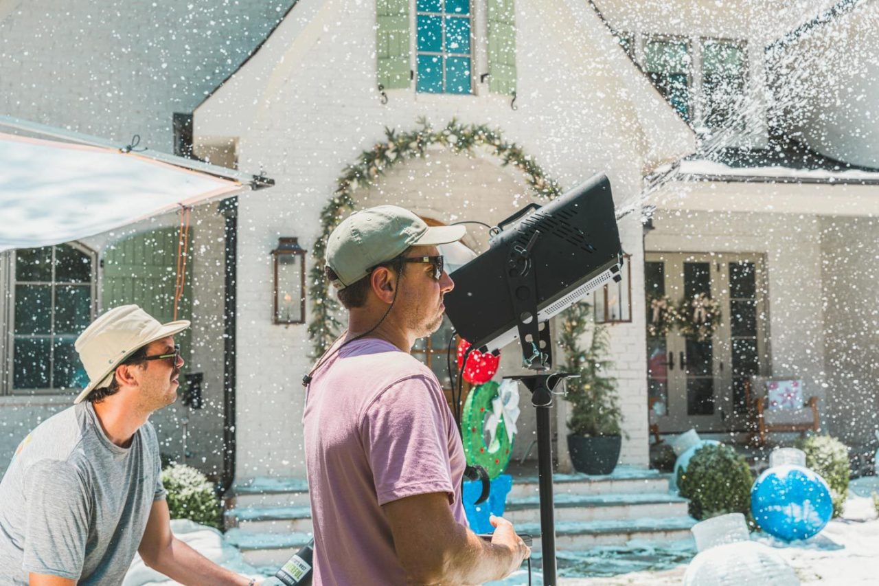 Lifestyle photography team on set arranging a shot of a house decorated with holiday lights and snow.