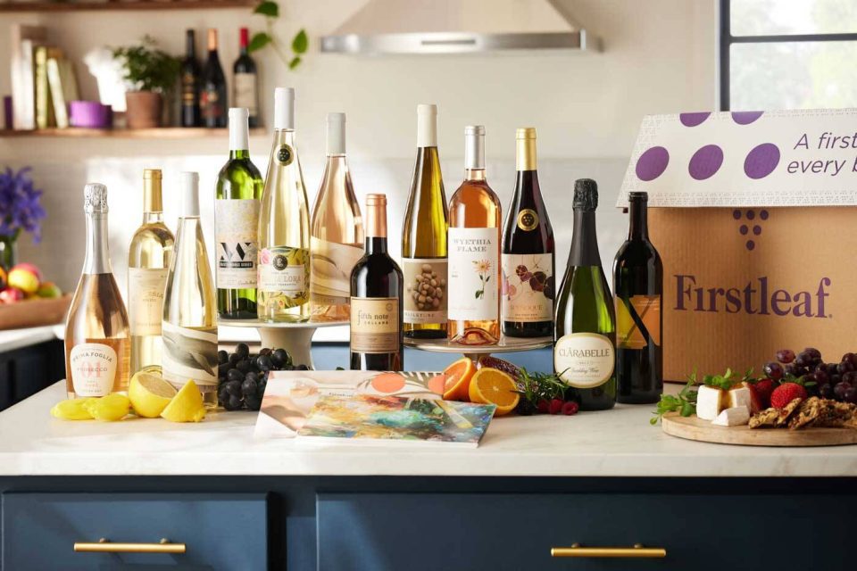 Photograph of colorful wine bottles on a kitchen counter island surrounded by fresh garnishes and citrus fruit.