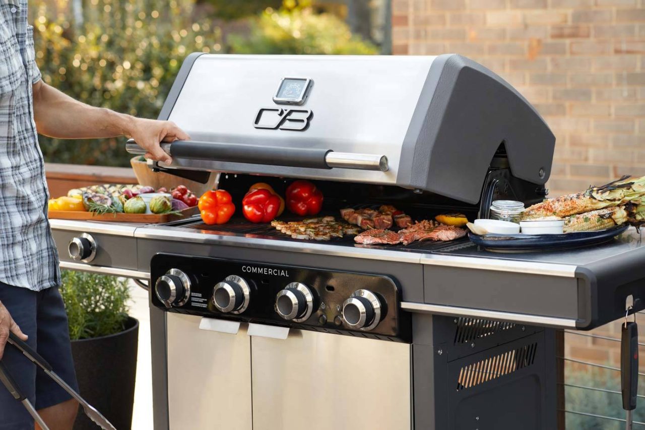 Photograph of a backyard grill with somebody opening the lid to reveal grilling meats and veggies..