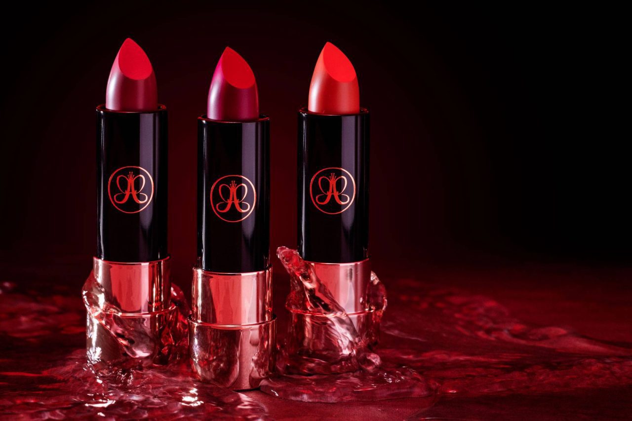 Dramatic product photo of red lipstick stood in a line against a black background.