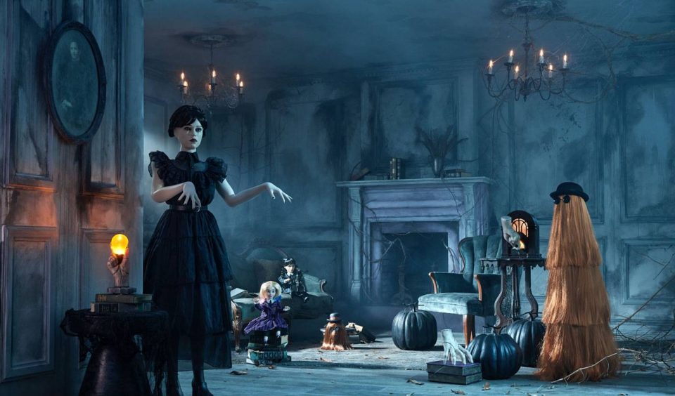 A dimly lit, eerie room with cobwebs and dusty furniture. A mannequin in a black dress stands amidst pumpkins, a doll, and a chest. An ominous figure, resembling Cousin Itt, is beside a fireplace. Chandeliers hang from the ceiling.