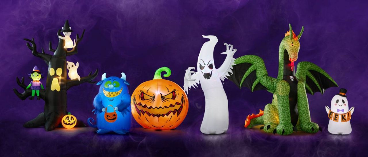 A lineup of Halloween-themed inflatables: a spooky tree with an owl and witch, a blue monster, a carved pumpkin, a ghost, a green dragon, and a ghost holding a "EEK" sign, all set against a purple smoky background.