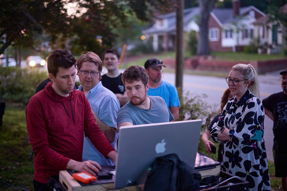 Creative team huddled around a laptop on an outdoor set on a suburban street.