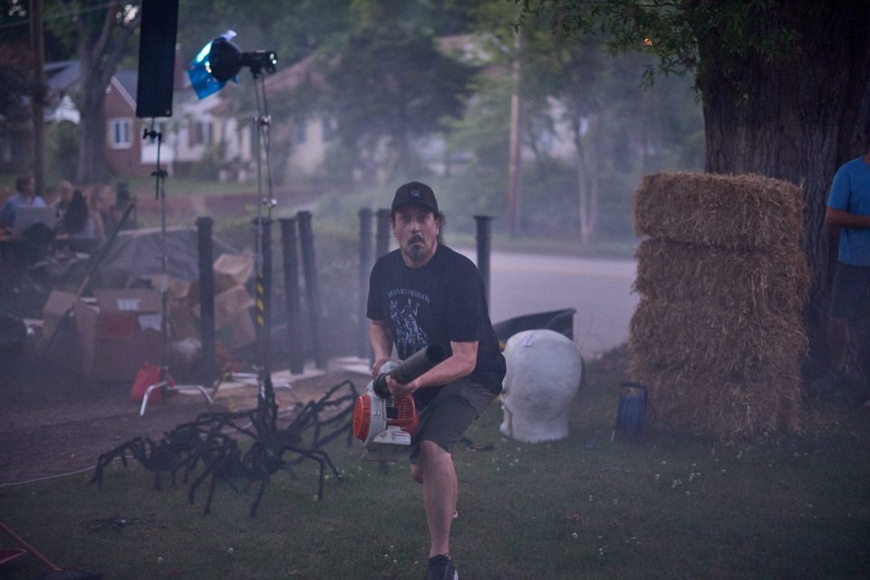 Crew member with leaf blower behind the scenes of a spooky outdoor Halloween set.