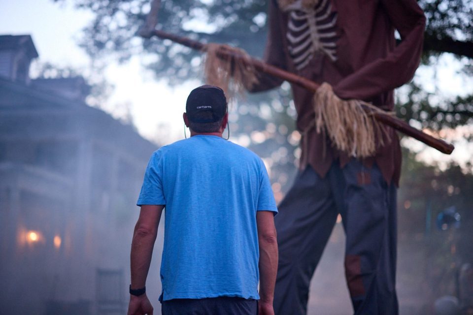 Crew member on a Halloween photoshoot set standing below a towering skeleton figure.