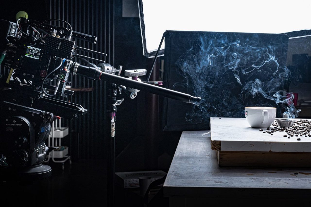 Photograph of a state-of-the-art camera pointed at smoky coffee beans and coffee mug arranged on a countertop.