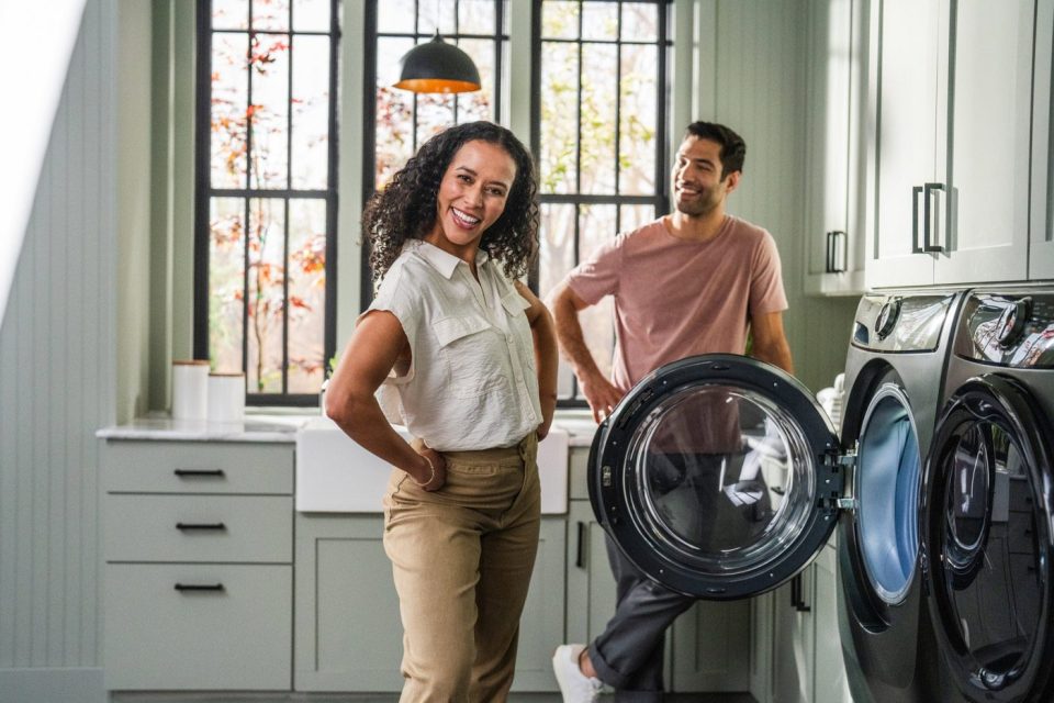 Lifestyle photograph of a couple smiling together while doing laundry in a laundry room.