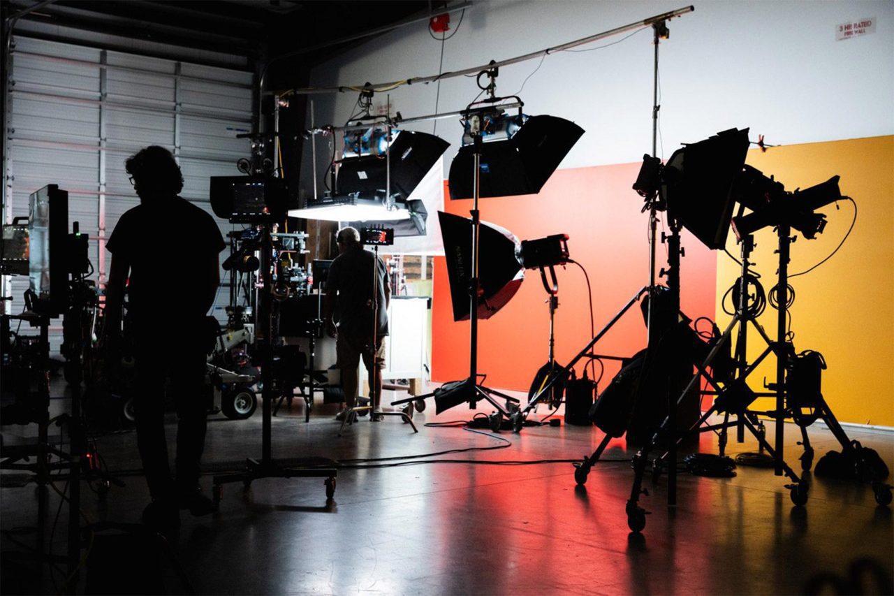 Set of photoshoot with cameras, stylists, and lights on a studio stage.