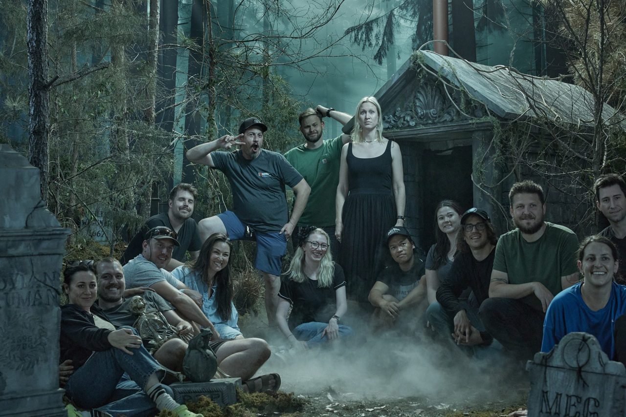 Group photograph of a creative team behind the scenes on a spooky graveyard set thick with fog.