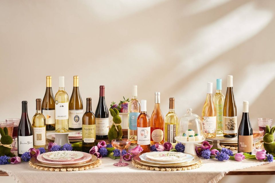 A table adorned with an assortment of wine bottles, including whites, reds, and rosés. The setting is accentuated with decorative flowers and elegant tableware, creating an inviting and festive atmosphere.