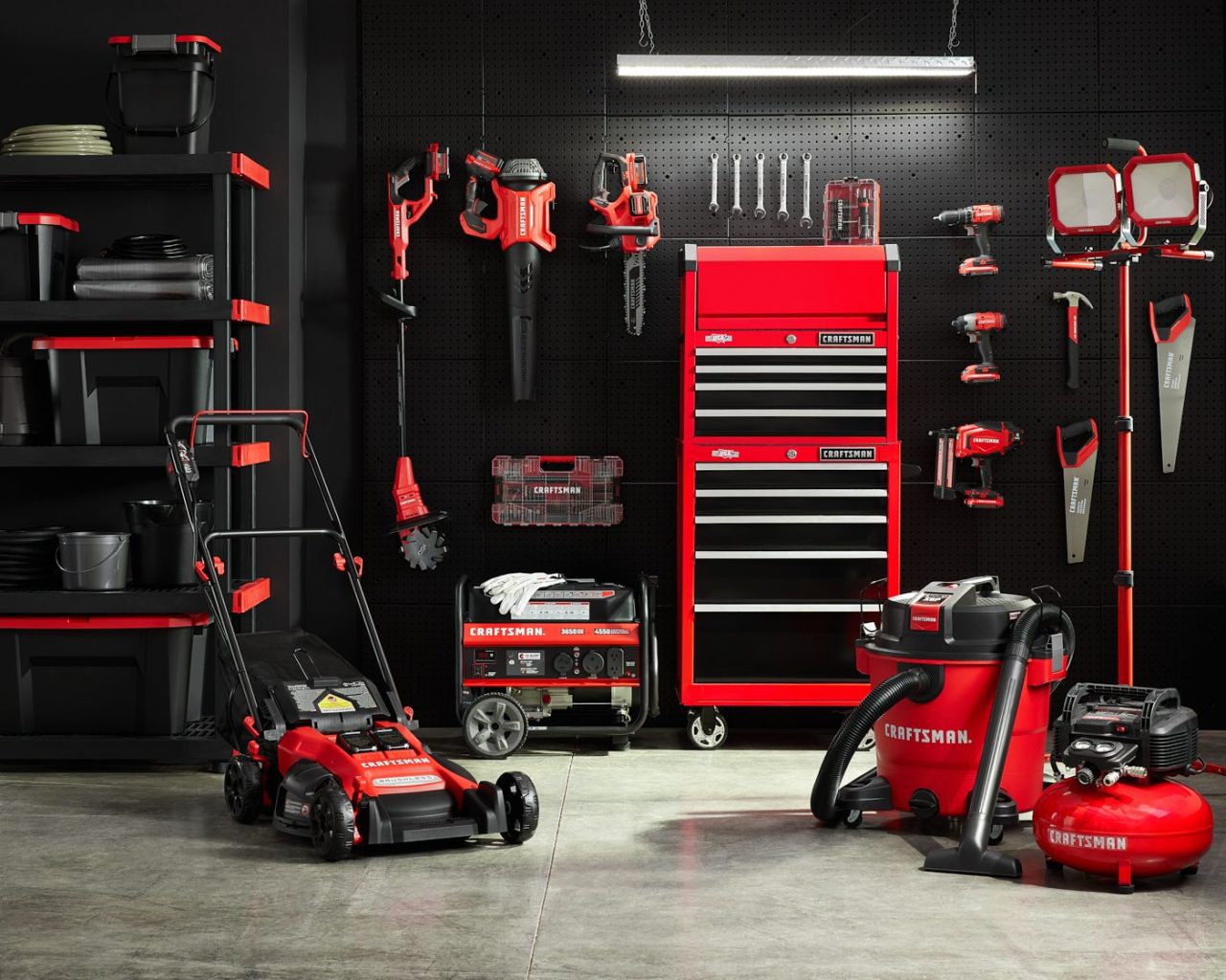 A well-organized garage features various Craftsman tools and equipment. There's a red toolbox, lawnmower, vacuum, and other tools neatly displayed against a black wall, with shelves on the left holding storage bins.