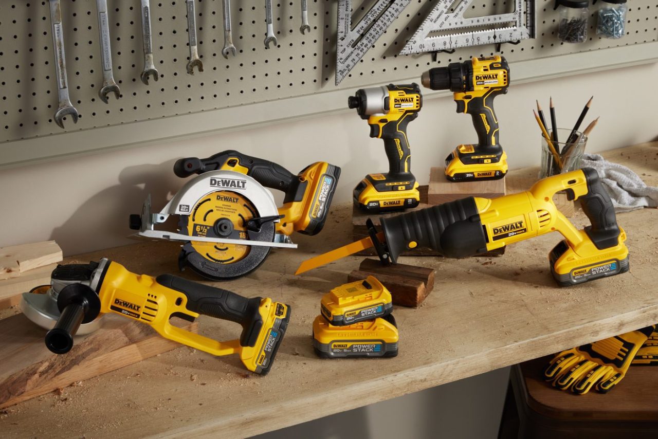 A workbench with various yellow and black power tools, including drills, a circular saw, a reciprocating saw, batteries, and measuring tools on a pegboard in the background.