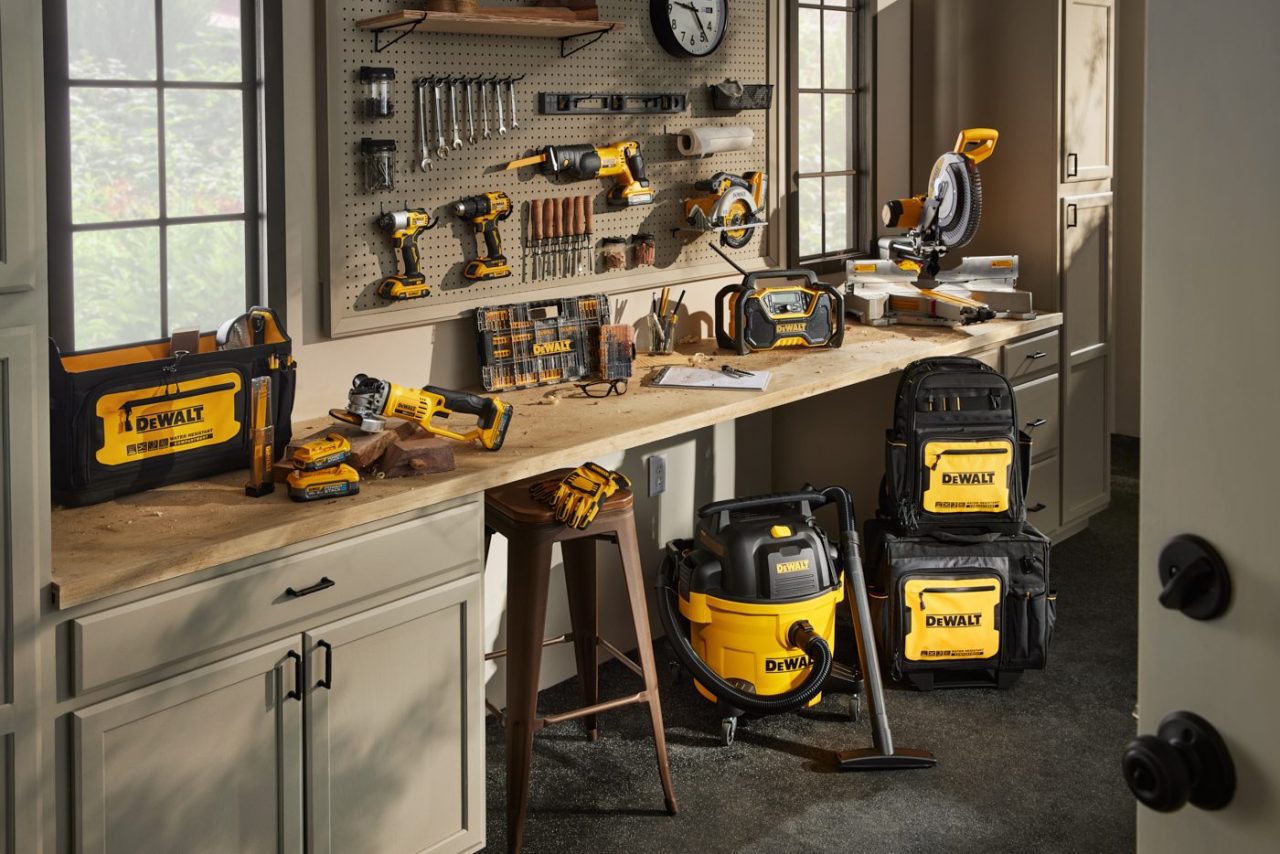 A workshop with DeWalt tools neatly arranged on a countertop, including drills, a saw, and a vacuum. A pegboard displays more tools. Sunlight filters through windows, illuminating the organized workspace.