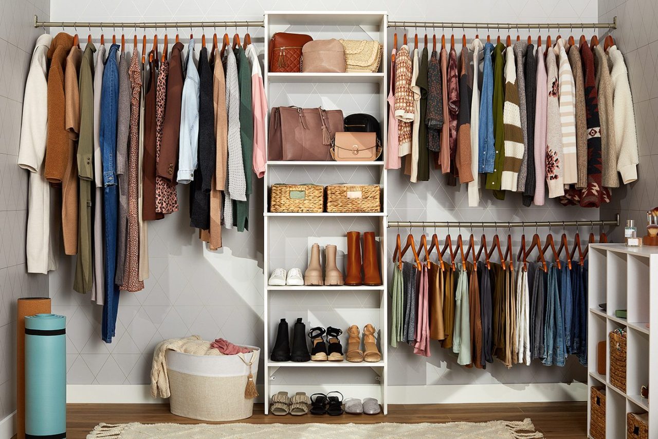 A neatly organized closet with hanging clothes, including shirts, sweaters, and dresses, in a range of colors. Shelves display bags, shoes, and baskets. A yoga mat and a laundry basket are placed on the floor.