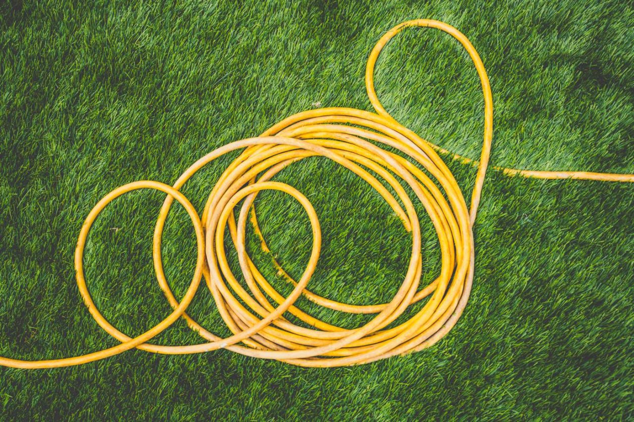 A yellow garden hose is coiled on a vibrant green grass surface. The hose loops into several circular formations, contrasting with the textured grass background.