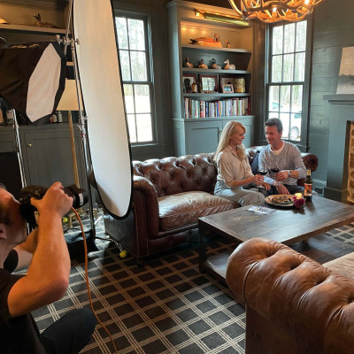 Photographer taking images of a home interior with a couple drinking wine.